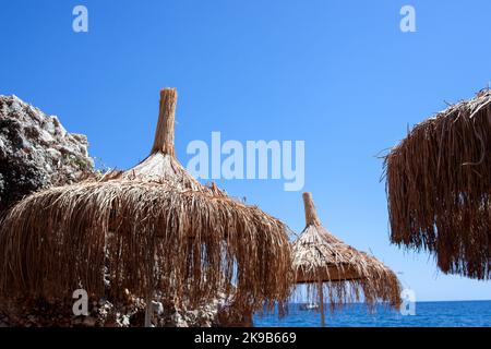 Strohschirm oder Strohhütte mit wunderschönem Blick auf den tropischen Strand. Strohschirme am Strand gegen klaren blauen Himmel Stockfoto