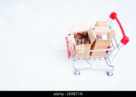 Kleine Pappkartons mit gerösteten Kaffeebohnen und Pappkaffeebechern in einem Miniatur-Schubkarren, isoliert auf weißem Hintergrund mit Platz für Kopien. Barist Stockfoto