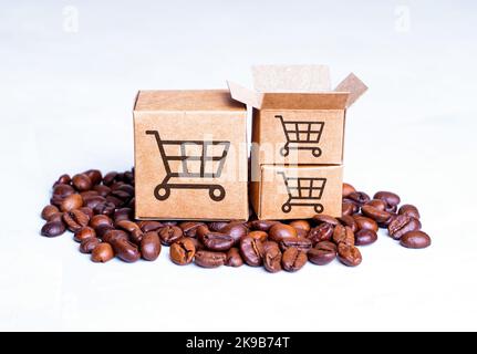 Stapel gerösteter Kaffeebohnen und Miniaturkartons mit Warenkorb-Symbolen oben isoliert auf weißem Hintergrund. E-Commerce und Kaffee liefern Stockfoto