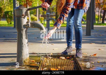 Junge Frau mit einer Handpumpe des öffentlichen Wasserraums. Stockfoto