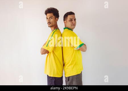 Black Brothers mit gelbem brasilianischem Hemd und Flaggenjubel isoliert auf Weiß. Fußballfans jubeln über den Sieg Brasiliens. Stockfoto