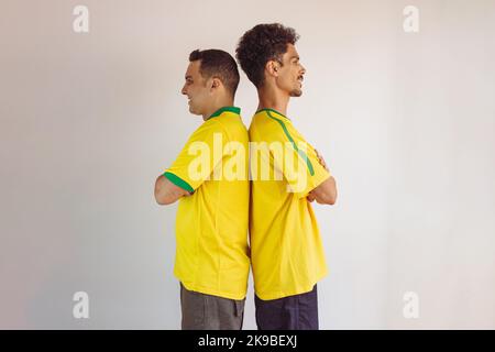 Black Brothers mit gelbem brasilianischem Hemd und Flaggenjubel isoliert auf Weiß. Fußballfans jubeln über den Sieg Brasiliens. Stockfoto