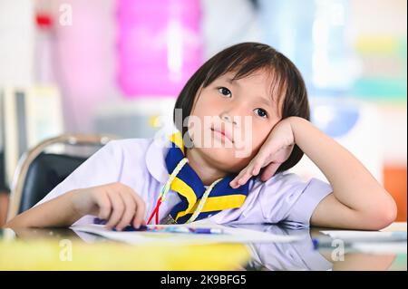 asiatische Student Mädchen traurig oder gelangweilt kleinen Schüler Mädchen in Uniform. Kind Lernprüfung im Klassenzimmer, gelöste Beispiele, Übungen in der Schule Arbeitsbuch Stockfoto