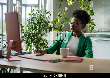 Konzentrierte afroamerikanische Managerin des erfolgreichen Startups sitzt am Computertisch im Büro Stockfoto