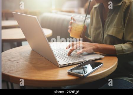 Frau, die mit einem Laptop arbeitete und Orangensaft im Café trank. Stockfoto