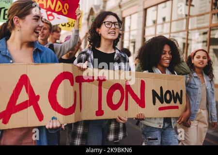 Gruppe multikultureller junger Menschen, die sich für den Klimaschutz in der Stadt einsetzen. Fröhliche Jugendaktivisten halten ein Banner, während sie gegen das Klima marschieren Stockfoto