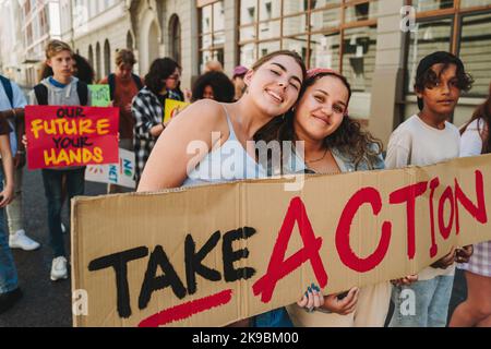 Glückliche Teenager-Mädchen mit einem Banner bei einem klimawechsel-marsch. Gruppe multikultureller Jugendaktivisten, die gegen die globale Erwärmung protestieren. Vielfältig Stockfoto