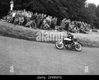 1954, historisch, ein männlicher Konkurrent auf einem Norton Motorrad auf der Rennstrecke Oliver's Mount Road in Scarborough, beobachtet von Zuschauern, die höher auf dem Kurs auf dem Rasen stehen, England, Großbritannien. Die hügelige Rennstrecke am Oliver's Mount ist Englands einzige natürliche „Road“-Rennstrecke und in dieser Zeit waren die Veranstaltungen als die Scarborough Races bekannt. Stockfoto