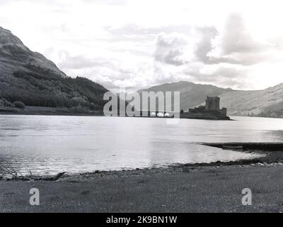 1956, historisches Bild, von einem Ufer eines loch, von Eilean Donan Castle, Western Highlands, Schottland, Großbritannien. Das Schloss oder die Festung liegt auf einer kleinen Gezeiteninsel an der Kreuzung von drei Seerochsen und wurde ursprünglich im 13. Jahrhundert erbaut, später zerstört und dann wieder aufgebaut und ist eine der berühmtesten in Schottland. Stockfoto