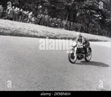 1954, historisch, ein männlicher Konkurrent auf einem Norton Motorrad auf der Rennstrecke Oliver's Mount Road in Scarborough, beobachtet von Zuschauern, die höher auf dem Kurs auf dem Rasen stehen, England, Großbritannien. Die hügelige Rennstrecke am Oliver's Mount ist Englands einzige natürliche „Road“-Rennstrecke und in dieser Zeit waren die Veranstaltungen als die Scarborough Races bekannt. Stockfoto