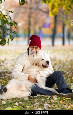 Vertikales Foto eines Mannes mittleren Alters und zweier Hunde, goldener Retriever beim Spaziergang im Stadtpark. Freundschaft und Pflege für Haustiere. Stockfoto