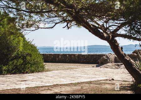 Korfu, Griechenland. Blick auf eine touristische Raststätte mit Betonsockel und Rand durch blaues Wasser. Grüne Büsche. Stockfoto