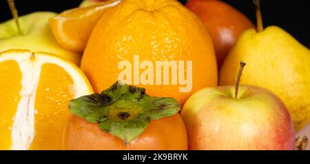Früchte von orangen und gelben Farben - Äpfel, Kaki, Birnen und Orangen auf schwarzem Hintergrund Stockfoto