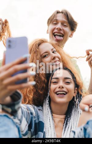 Portrait von aktiven jungen Menschen, die zusammen ein Selfie machen und in einer lustigen Position stehen und verschiedene Mimik machen, die zusammen Spaß haben. Sommer Stockfoto