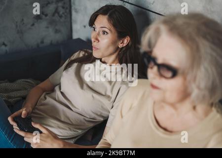 Porträt einer reifen Frau, die sich wundert, wie gut ihre alte Mutter Videospiele spielt. Großmutter und Joystick. Oma spielen Videospiele. Stockfoto