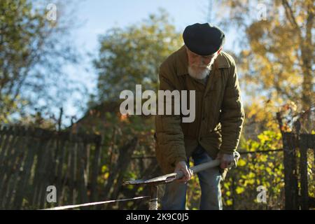 Russischer alter Mann im Garten. Opa arbeitet an Land. Rentner arbeiten. Mann über 90 Jahre alt. Stockfoto