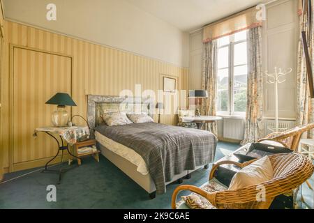 Stilvolle Lampe, die auf einem alten Nachttisch mit Büchern und Zeitschriften am Bett leuchtet Stockfoto