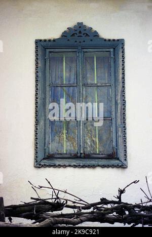 Kreis Gorj, Rumänien, ca. 2000. Einfaches Holzfenster eines traditionellen alten Hauses, mit wunderschönen, handgeschnitzten Zierleisten. Stockfoto