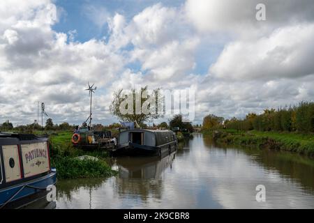 Traditionelle schmale Boote und Lastkähne mit einer kleinen Windmühle, um die Heizung usw. anzutreiben, an Anlegestellen am Kennet und Avon Canal nahe Seend, England. Stockfoto