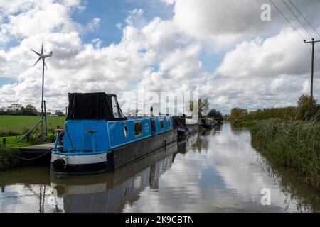 Traditionelle schmale Boote und Lastkähne mit einer kleinen Windmühle, um die Heizung usw. anzutreiben, an Anlegestellen am Kennet und Avon Canal nahe Seend, England. Stockfoto