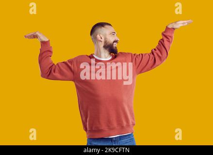 Fröhlicher Mann, der Spaß hat und auf orangefarbenem Hintergrund im Studio herumtanzt. Stockfoto