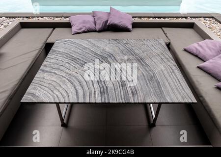 Gestreifter Esstisch aus Granit mit Kissen auf dem Sofa am Pool Stockfoto