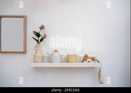 Minimalistisches Wohnzimmer mit Blume in Vase, Keramik-Topf, Tasse, Kamera-Mockup und leeren Holz Bilderrahmen auf weißen Holzwand Stockfoto