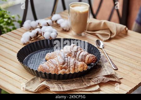 Französisches Frühstück: Pulverförmige Croissants mit einem Glas Latte im Freien Stockfoto