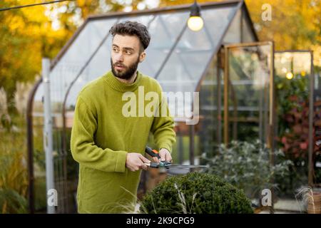 Guy schneidet einen runden Busch mit einer Schere Stockfoto