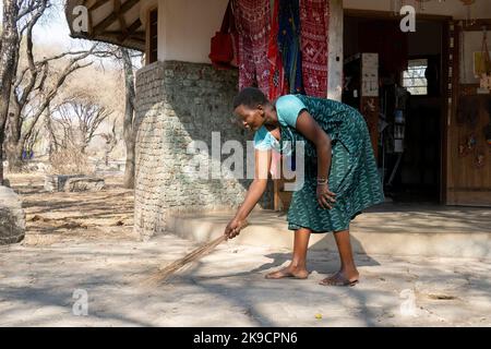 Tarangire, Tansania - 12.. Oktober 2022: Eine tansanische Frau, die mit einem traditionellen Besen vor ihrem Souvenirladen fegt. Stockfoto