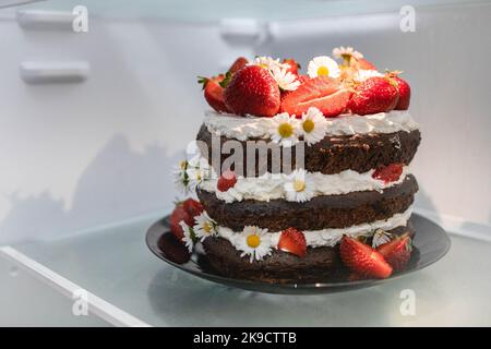 Schokoladen-Erdbeer-Herzkuchen mit Kamillenblumen-Dekoration im Kühlschrank. Stockfoto