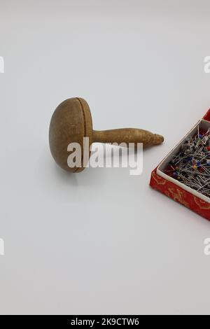 Nähen von Accessoires auf weißem Hintergrund. Stifte in einer Schachtel und ein Holzpilz, mit dem Löcher auf Kleidung, Strumpf oder Socken befestigt werden Stockfoto