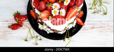 Schokoladen-Erdbeer-Herzkuchen mit Kamillenblumen-Dekoration. Bannerformat Stockfoto