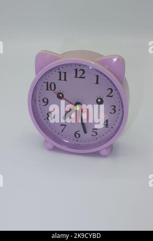 Lila Flieder farbige Uhr in Ferkel-Form auf weißem Hintergrund Stockfoto