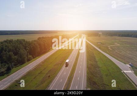 Transportlogistik. Draufsicht auf Lastwagen und Autos, die sich in den Strahlen des Sonnenuntergangs entlang einer asphaltierten Straße bewegen. Hintergrundbild, Bereich außerhalb des Fokus. Dreharbeiten Stockfoto