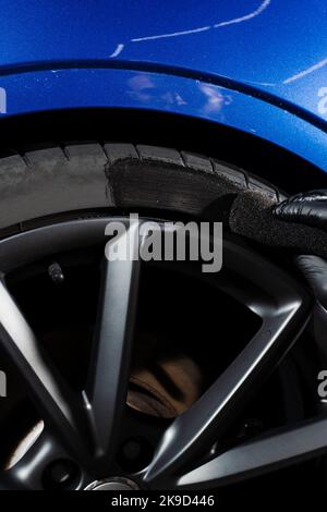 Schwärzung des Reifenrades des Autos mit Schwamm mit chemischer Schwärzung des Gummis in Detaillierung Auto-Service. Vertikales Foto für soziale Medien Stockfoto