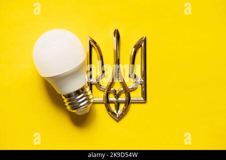 LED-Lampe und Wappen der Ukraine auf gelbem Grund, Ukraine ohne Licht, Energiekrise, Krieg 2022 Stockfoto