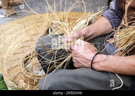 Nahaufnahme in horizontaler Ansicht der Hände eines Korbherstellers, die zeigt, wie Körbe und Weidenprodukte hergestellt werden. Bastelkonzept Stockfoto