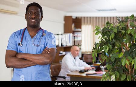 Professioneller afroamerikanischer Arzt, der im medizinischen Büro steht Stockfoto