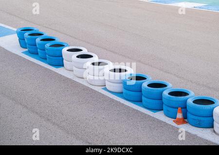 Alte, weiß und blau lackierte Reifen, gestapelt am Rand einer Kart-Rennstrecke, Asphalt einer Rennstrecke mit gebrauchten Reifen an den Rändern, Reifen verwendet für Stockfoto