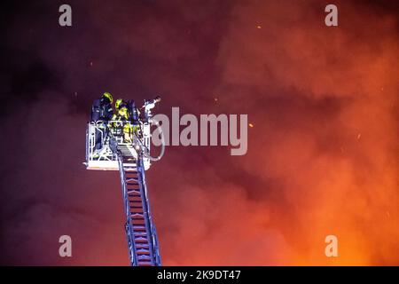 Bad Oeynhausen, Deutschland. 28. Oktober 2022. Die Feuerwehrleute stehen auf einem Kran auf dem Gelände eines Entsorgungsunternehmens, in dem die Halle für gefährliche Abfälle in Brand steht. Quelle: Lino Mirgeler/dpa/Alamy Live News Stockfoto