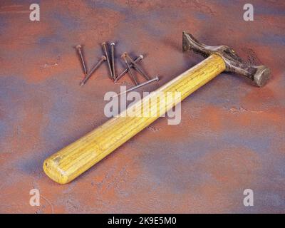Ein alter Hammer mit einem Holzgriff und einem Haufen rostiger Nägel auf einem grunge-artigen Hintergrund Stockfoto