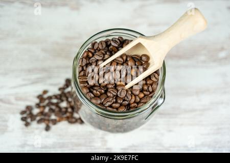 Kaffeebohnen, die natürlich in einem antiken Glasgefäß und einem Holzlöffel geröstet werden, um sie aufzunehmen. Stockfoto