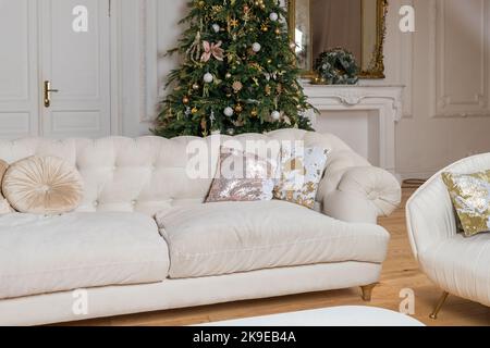 Luxuriöse, glänzende und klassische Kissen auf beigem Sofa. Dekorative, Pailletten- und beigefarbene Wildlederkissen auf der Couch. Dekoration des Zimmers für den Urlaub Stockfoto