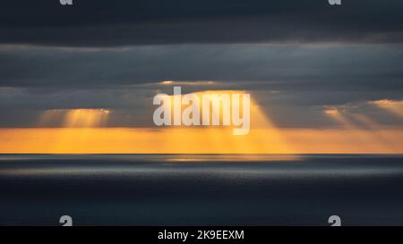 Krepuskuläre Lichtstrahlen, die durch Wolken über dem Ozean leuchten Stockfoto