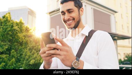 Der Start in den freien Tag mit einigen guten Nachrichten. Ein hübscher junger Geschäftsmann, der sein Handy benutzt, während er durch die Stadt läuft. Stockfoto
