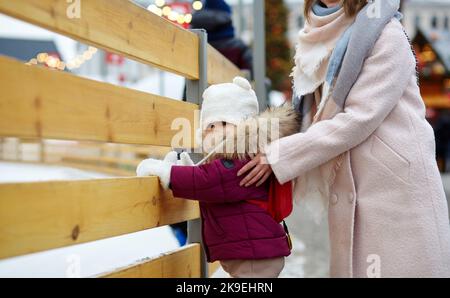 Mutter und Tochter laufen an Weihnachten und Neujahr durch die Stadt. Eltern und kleine Kinder haben Spaß im Freien Stockfoto