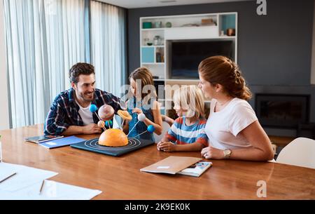 Unser Kapitän führt den Weg. Eine schöne junge Familie, die zu Hause an einem wissenschaftlichen Projekt arbeitet. Stockfoto