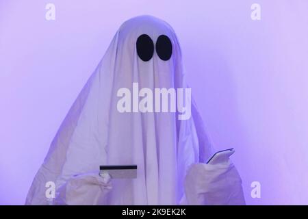 ghost Halloween verwendet Mobiltelefone, um im Internet zu surfen, um Online-Shops und Märkte zu durchsuchen. Der Geist macht eine Bestellung von einem Smartphone für Halloween. Ghost bezahlt den Online-Kauf per Kreditkarte, Bankkarte. Stockfoto