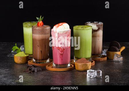 Süße Milchshakes mit Schokolade, Karamell, Erdbeere und Schlagsahne auf einem Holzbrett auf dem Tischhintergrund. Stockfoto